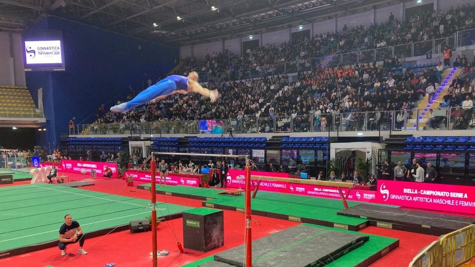 Un esercizio alla sbarra e, sullo sfondo, la tribuna gremita